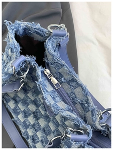 Detailed macro shot of distressed blue denim fabric and silver zipper of a tote bag