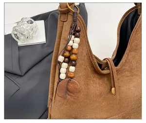Detail of brown suede shoulder bag with bohemian wood bead charm and contrast stitching