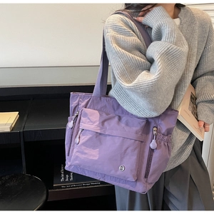 Detailed side view of lavender nylon tote bag with multiple zipper pockets on model
