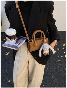 Brown leather mini tote bag detail with plush bunny charm in an urban street style