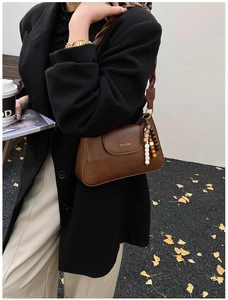 Detail of a dark brown faux leather baguette bag with woven strap and beaded charm