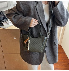 Detail der grauen Beuteltasche mit Karomuster, Perlenanhänger und Ledergriffen