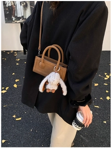 Brown suede crossbody bag with plush bunny accessory on autumn gingko leaf ground