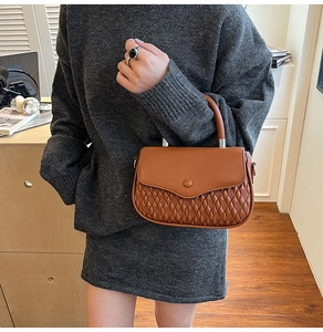 Detail of caramel brown crossbody bag featuring woven texture and smooth metal handles