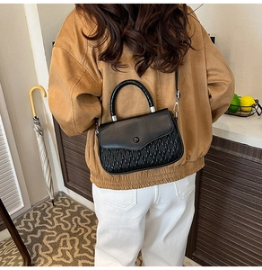 Detail of black leather crossbody bag with woven texture worn by model in a modern room