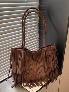 Borsa tote marrone con frange in finta pelle scamosciata su sfondo di una finestra elegante