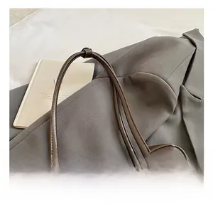 Detail of dark brown leather pillow bag with debossed logo and beaded charm on gray blazer