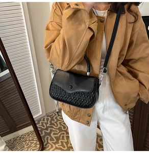 Detail of black crossbody bag featuring quilted texture and round metal buckle on model