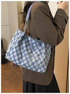 Detail of blue checkerboard denim tote with frayed edges and leather chain strap