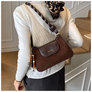 Detail of retro brown suede handbag with woven strap and ethnic beaded charm accessory