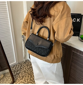 Detail of black crossbody bag with pleated texture and curved handle worn by a model