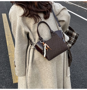 Detail der dunkelbraunen Leder-Eimertasche mit Metallgriff und Ethno-Perlenanhänger