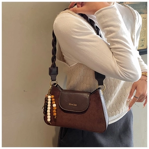 Detail of a brown suede crossbody bag with woven strap and beaded charm decoration