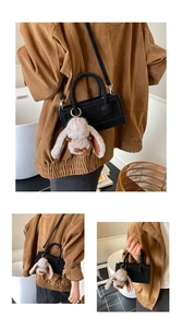 Close-up of black small square bag with plush bunny pendant and slim crossbody strap