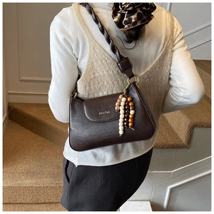 Dark brown underarm bag with braided strap and beaded tassel detail on a shoulder