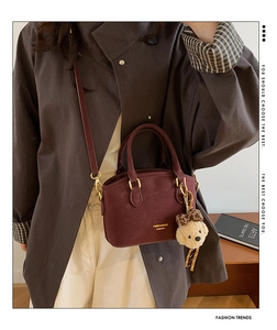 Detail of burgundy crossbody bag with golden hardware and cute bear plush charm