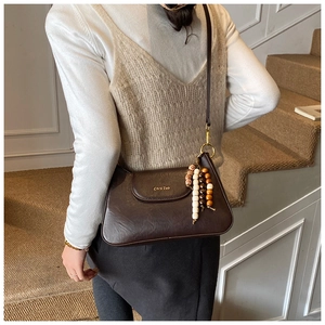 Detail of caramel brown leather shoulder bag with vintage bead charm on an elegant strap