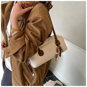 Close-up detail of cream shoulder bag with vintage wood bead charm and brown strap