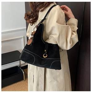 Detail of black suede shoulder bag with white contrast stitching and bead charm