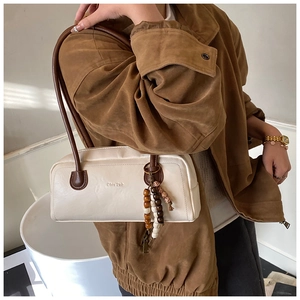 Detail of a retro cream Boston bag with wooden bead charm and long brown shoulder strap