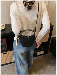 Primer plano de un bolso bandolera negro mate con cuentas de madera y borla de cuero