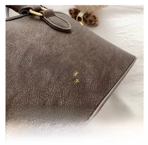 Detail of dark brown lychee leather handbag with gold logo and brass ring hardware