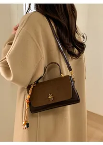 Detail of dark brown matte leather crossbody bag with vintage gold clasp and bead charm