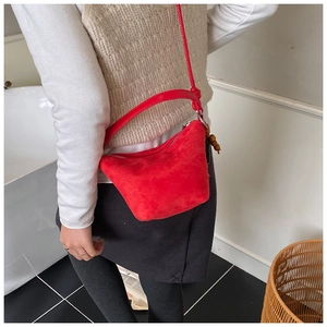 Detalle de bolso tipo cubo de ante rojo con correa anudada y adornos de cuentas de madera