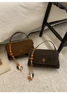 Detail of vintage flap handbag in suede texture with wooden bead tassel on white rug