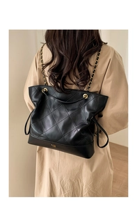 Detail of black quilted tote bag with gold chain strap on light trench coat