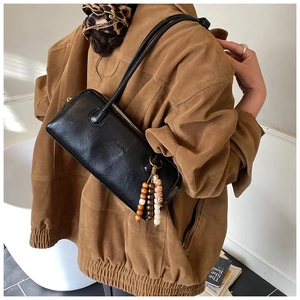 Detail of black pebbled leather underarm bag featuring vintage beaded tassel charm