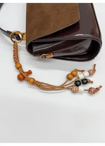Detail of vintage shoulder bag featuring burgundy leather with a colorful beaded tassel