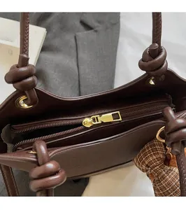 Close-up of smooth gold zipper hardware and knotted strap on dark brown leather bucket bag