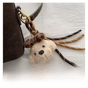 Detail showing a plush teddy dog charm with leopard bow on a brown leather shoulder bag