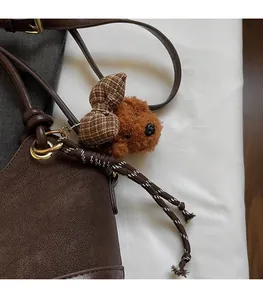 Brown plush puppy bag charm with checkered bow on dark brown leather handle close-up