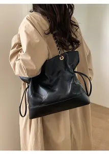 Detail of black quilted leather tote bag with metal chain strap and golden logo