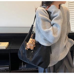 Detail of black suede tote bag with plush bear charm worn by a model in a library