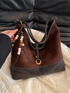 Dark brown suede tote bag with contrast stitching and decorative wooden beads on a sofa