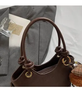 Detail of dark brown lychee textured handbag with knot strap and gold ring hardware