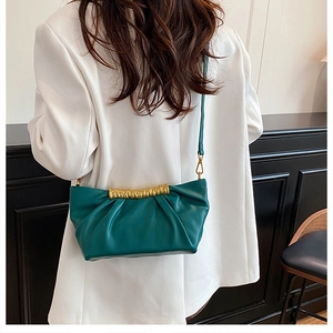 Detail of dark green pleated crossbody bag with gold metal trim styled on white suit