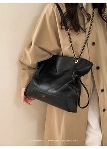 Detail of quilted black tote bag with gold chain strap and minimalist logo