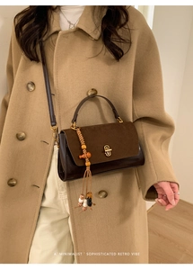 Detail of retro dark brown leather handbag featuring a gold buckle and woven bead pendant