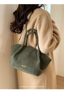 Close-up of dark green suede tote bag with golden metal trim and sleek shoulder strap