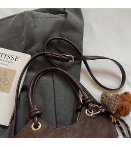 Detail of adjustable strap and brown teddy bear charm on textured leather bucket bag
