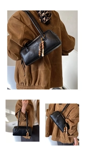 Close-up of black leather underarm bag with decorative wooden beads and embossed logo