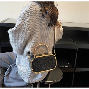 Detail of black quilted leather handbag with gold textured metal handle on display