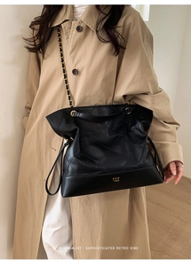 Detail of black quilted leather tote bag with gold chain strap on a khaki trench coat