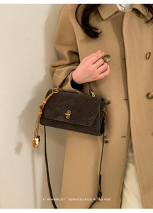 Close-up of matte grey tote bag with gold lock and beaded tassel on wool coat
