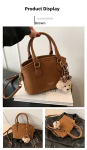 Detail of brown suede handbag with dual handles, adjustable strap and bear charm