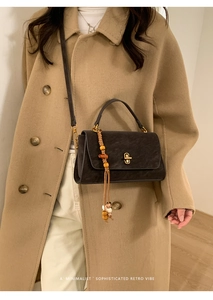 Close-up of retro matte black square bag with golden lock and beaded ethnic pendant